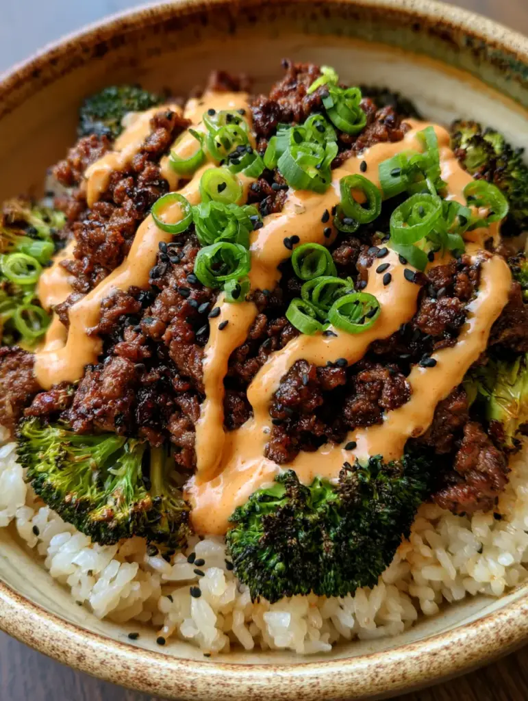 Bowl de cerámica rústica con capas de arroz, carne con brócoli y salsa sriracha en zigzag.