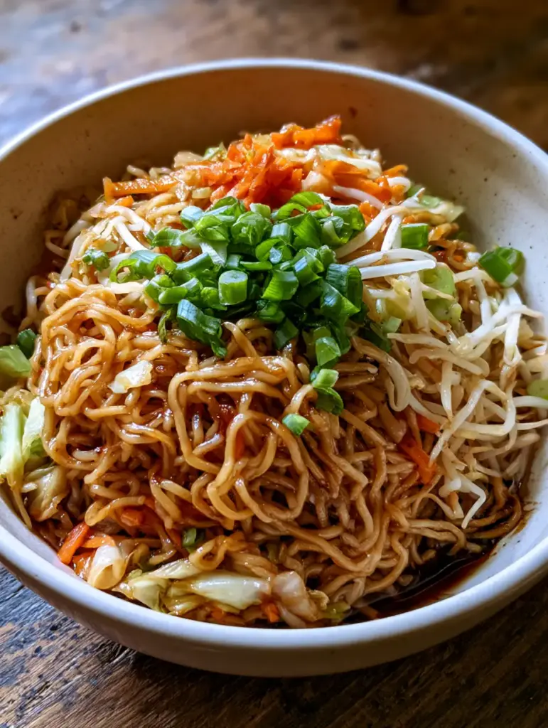 Detalle de fideos chow mein casero con glaseado oscuro y cebolletas verdes brillantes.