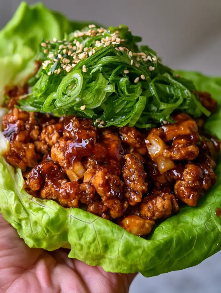 Wraps de Pollo Estilo Oriental con Lechuga Crujiente y Salsa Hoisin 2 Vista de cerca de un wrap de pollo humeante con salsa hoisin oscura y brillante sobre hojas de lechuga verde vibrante.