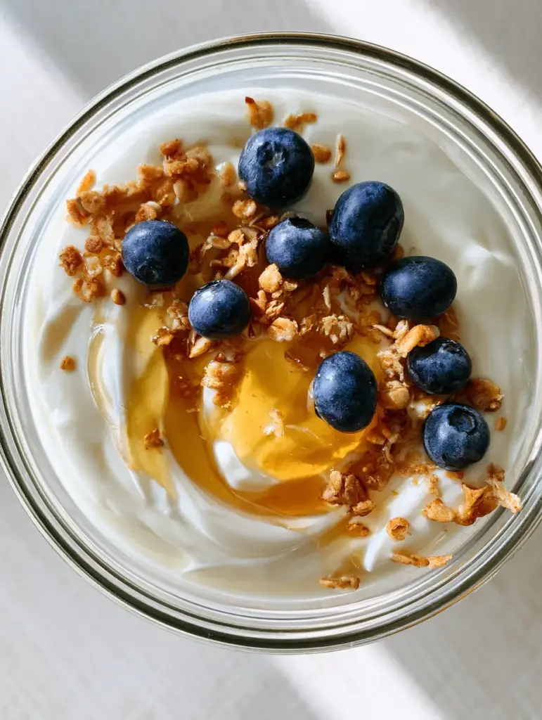 Vista cenital de un bol de cristal con yogur casero ultra espeso, decorado artísticamente con granola y menta. (yogur casero)