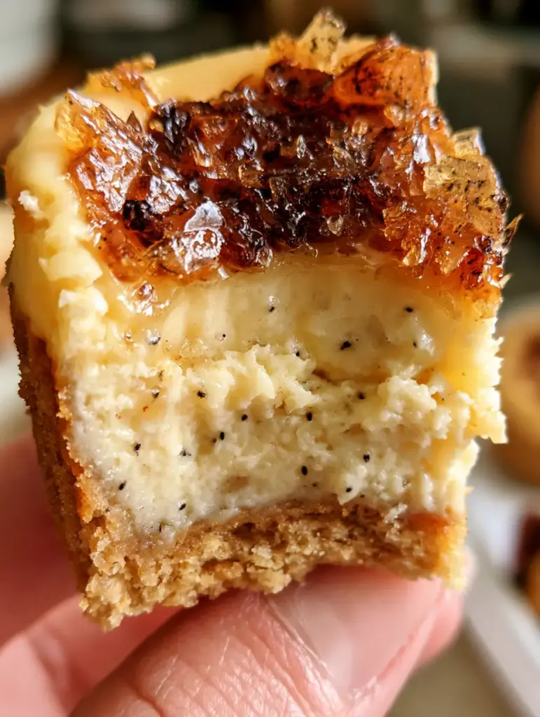 Mano sosteniendo un cupcake de cheesecake con capa superior de caramelo ámbar oscuro tipo cristal roto.