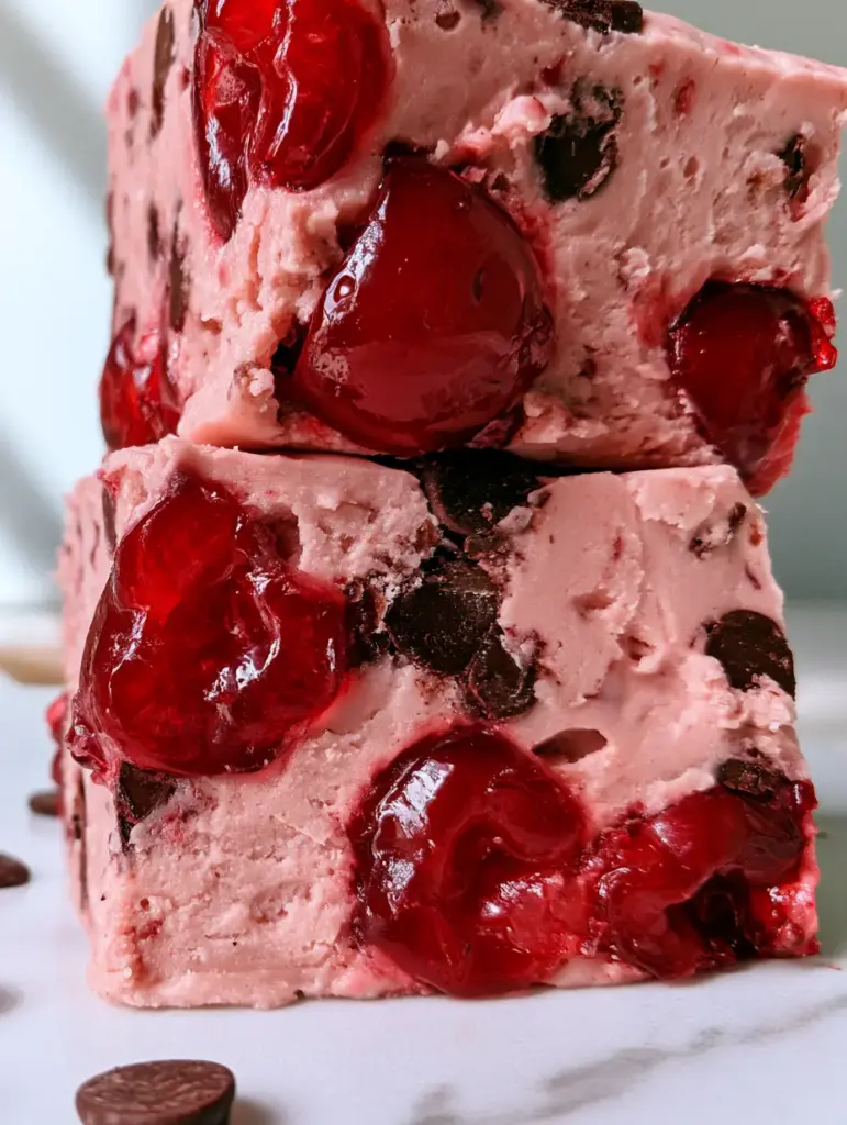 Cuadrados de fudge de cereza con superficies de corte lisas sobre una mesa de mármol blanco.